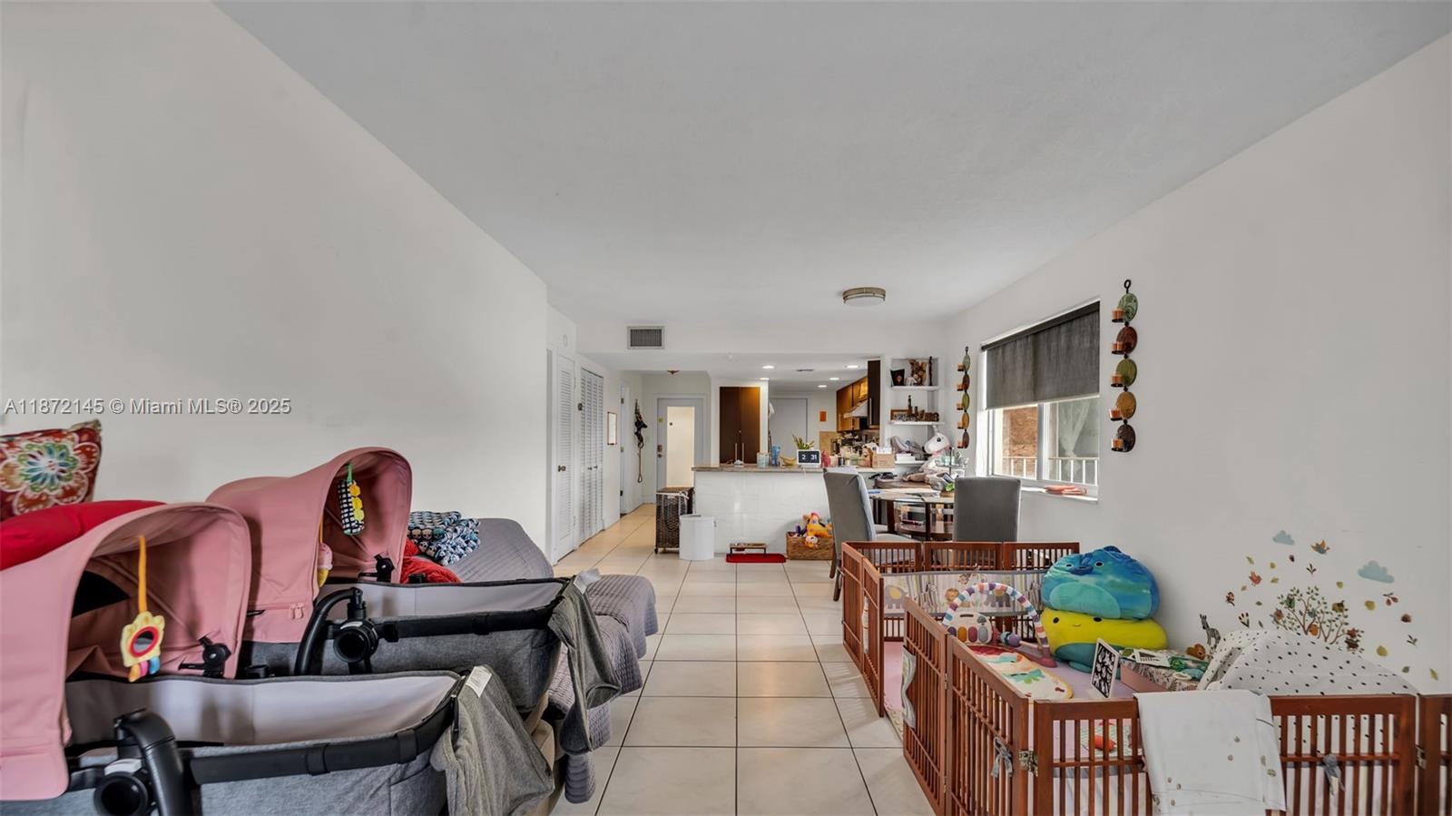 A living area with tile floors, a playpen, and a stroller facing the kitchen — 8001 Crespi Blvd # 4B, Miami Beach FL 33141, MIAMI BEACH, FL