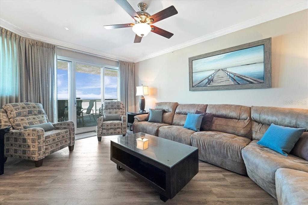 A living room features a brown sectional, patterned armchairs, a glass coffee table, and balcony views — 1925 S ATLANTIC AVENUE UNIT 502, DAYTONA BEACH, FL
