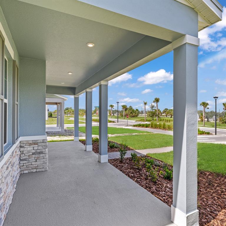 A covered front porch features gray columns, stone accents, and recessed lighting overlooking a neighborhood — 4712 INNER WORLD LANE, WESLEY CHAPEL, FL