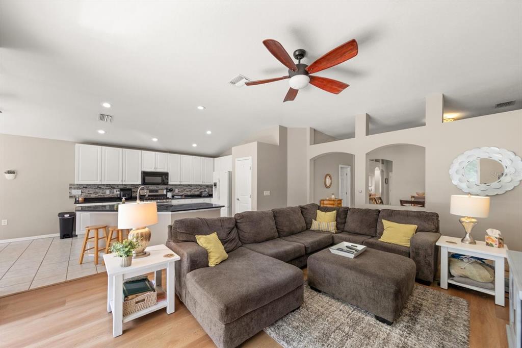 A living room with a sectional sofa and an open kitchen with white cabinets — 4422 HAVELOCKE DRIVE, LAND O LAKES, FL