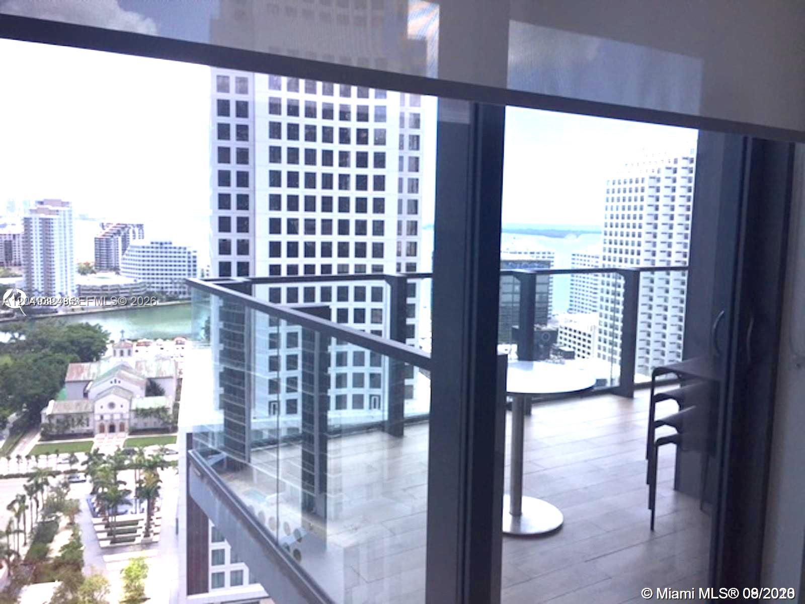 A balcony with a glass railing overlooks a city skyline and a nearby church — 68 SE 6th St # 2007, Miami FL 33131, MIAMI, FL