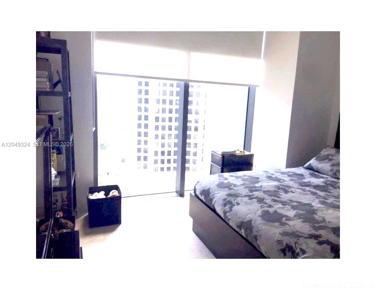 A bedroom features a bed with patterned bedding, a tall shelving unit, and floor-to-ceiling windows — 68 SE 6th St # 2007, Miami FL 33131, MIAMI, FL