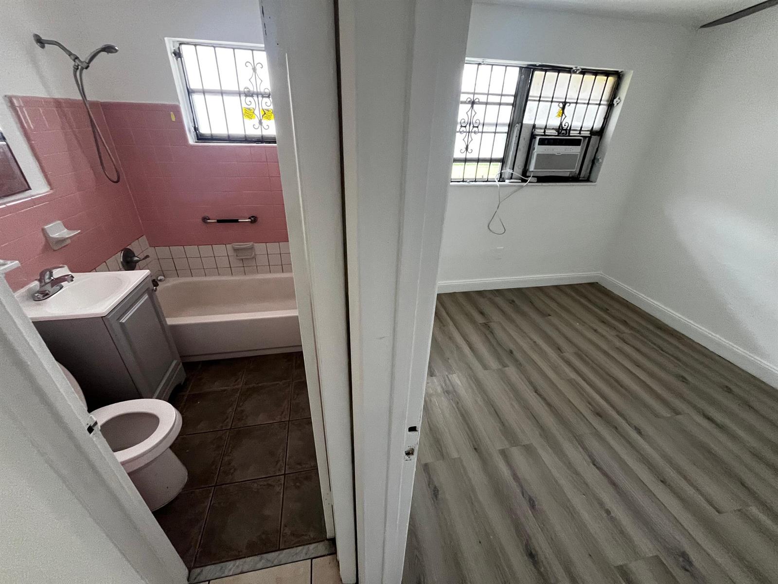 A bathroom with pink tile and a bathtub sits beside a room with wood flooring — 3015 NW 8th Avenue # 11, Miami FL 33127, MIAMI, FL