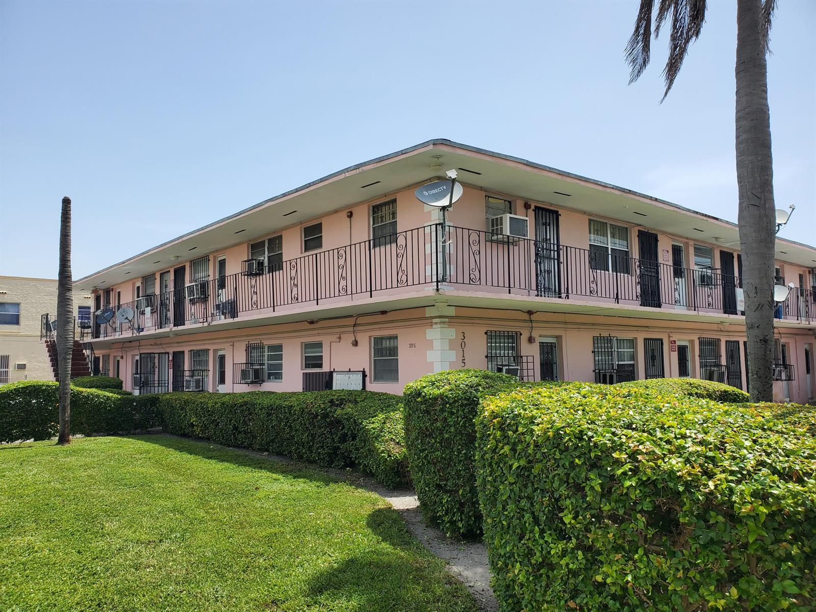 A two-story pink apartment building features exterior walkways with black railings and manicured hedges — 3015 NW 8th Avenue # 11, Miami FL 33127, MIAMI, FL