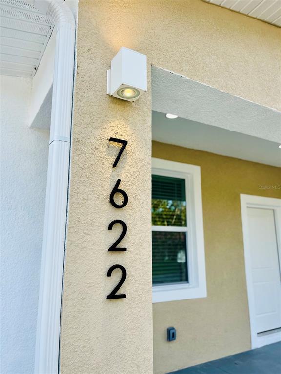The exterior wall of a house features a vertical address number and a light fixture — 7622 CYPRESS DRIVE, NEW PORT RICHEY, FL