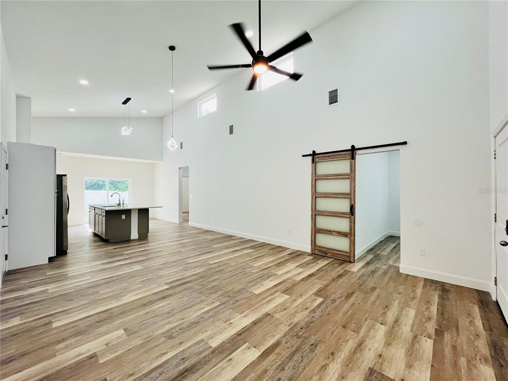 An open-concept living area features high ceilings, wood-look flooring, a ceiling fan, and a barn door — 7622 CYPRESS DRIVE, NEW PORT RICHEY, FL