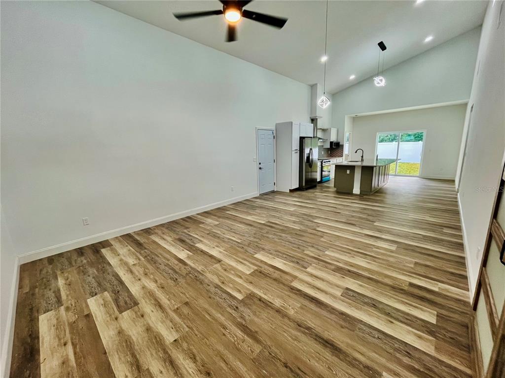 A spacious open-concept living area features vaulted ceilings, wood-look flooring, and a modern kitchen island — 7622 CYPRESS DRIVE, NEW PORT RICHEY, FL