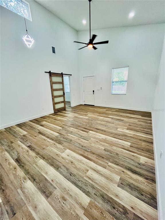 A high-ceilinged room features wood-look flooring, a ceiling fan, a barn door, and white walls — 7622 CYPRESS DRIVE, NEW PORT RICHEY, FL