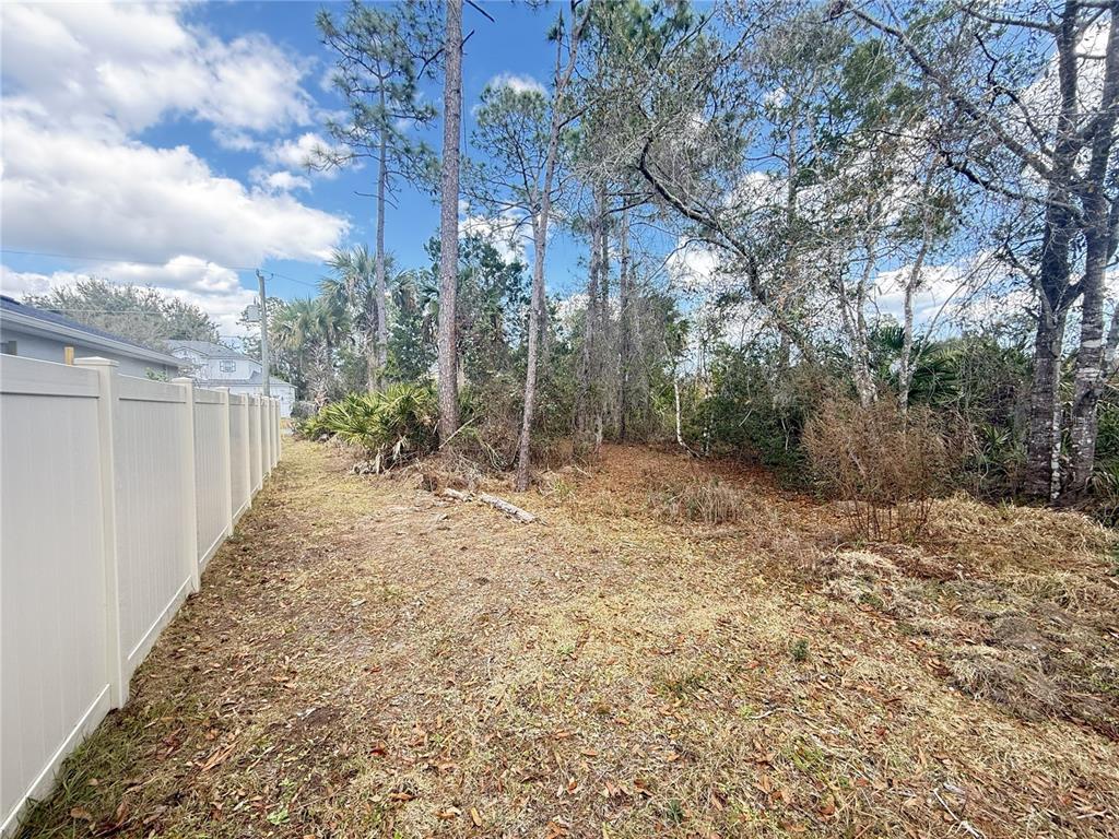 A view of a grassy, wooded backyard lot bordered by a white vinyl fence — 12 PINEASH LANE, PALM COAST, FL