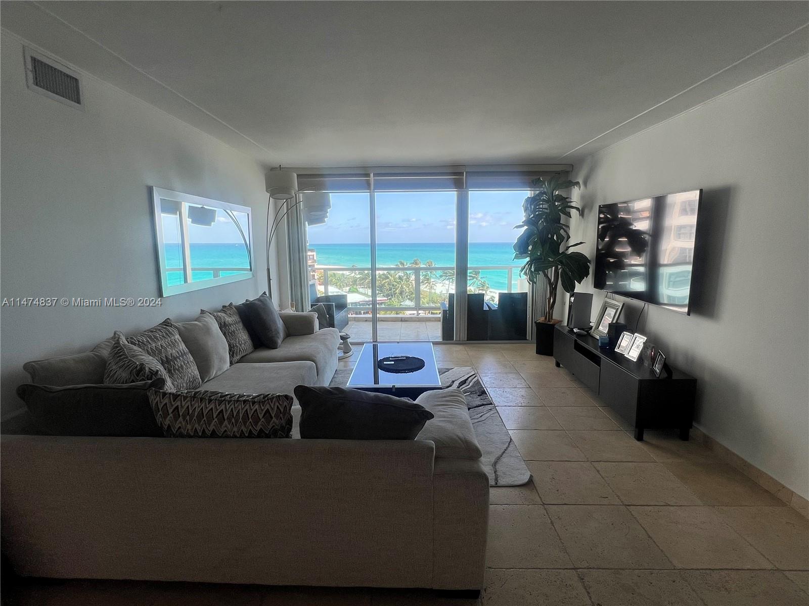 A living room features a sectional sofa, a television, and a balcony overlooking the ocean — 5151 Collins Ave # 1035, Miami Beach FL 33140, MIAMI BEACH, FL