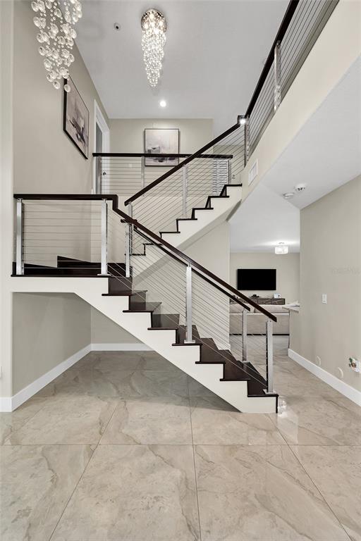 A modern staircase with dark wood treads and cable railings sits in a tiled foyer — 1385 SW 143RD COURT, MIAMI, FL
