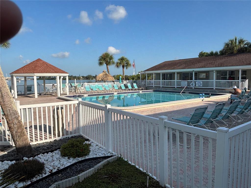 A swimming pool area features lounge chairs, a gazebo, and a building near the water — 3640 41ST LANE S UNIT 72E, ST PETERSBURG, FL