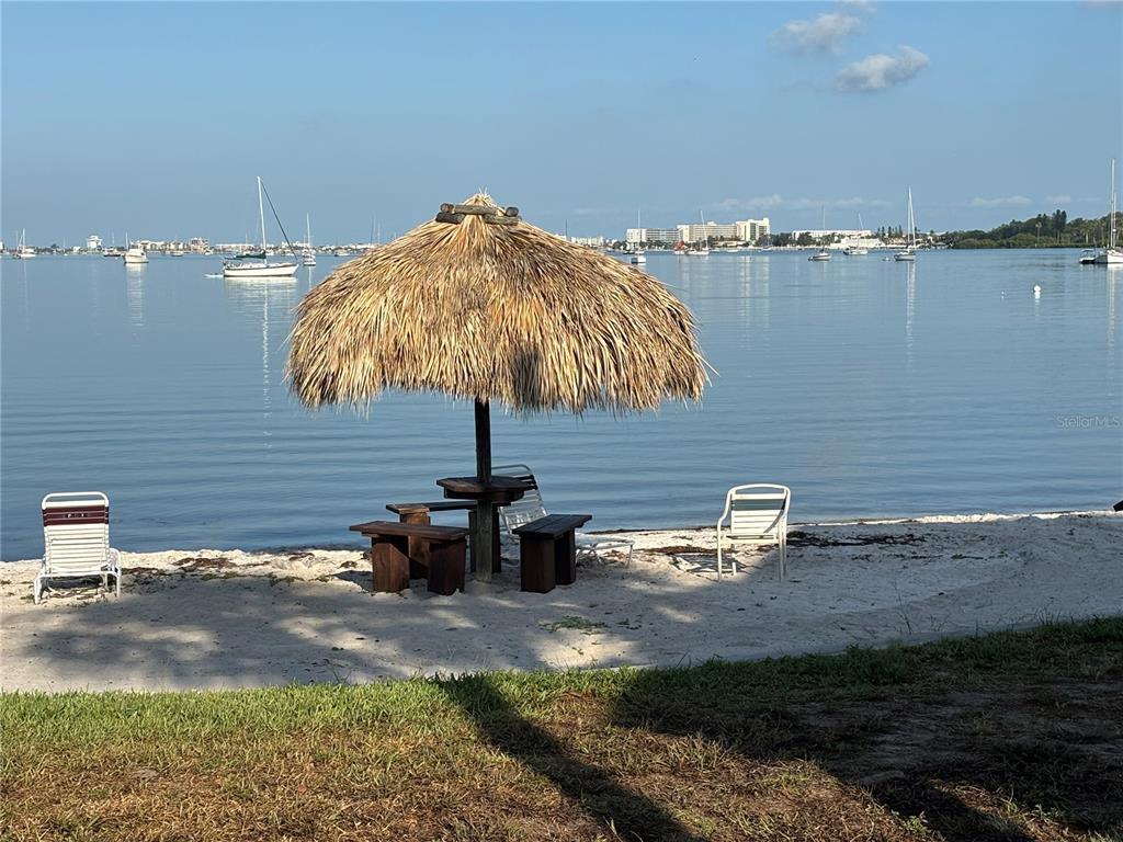 A thatched-roof tiki hut with benches sits on a sandy beach overlooking a bay — 3640 41ST LANE S UNIT 72E, ST PETERSBURG, FL