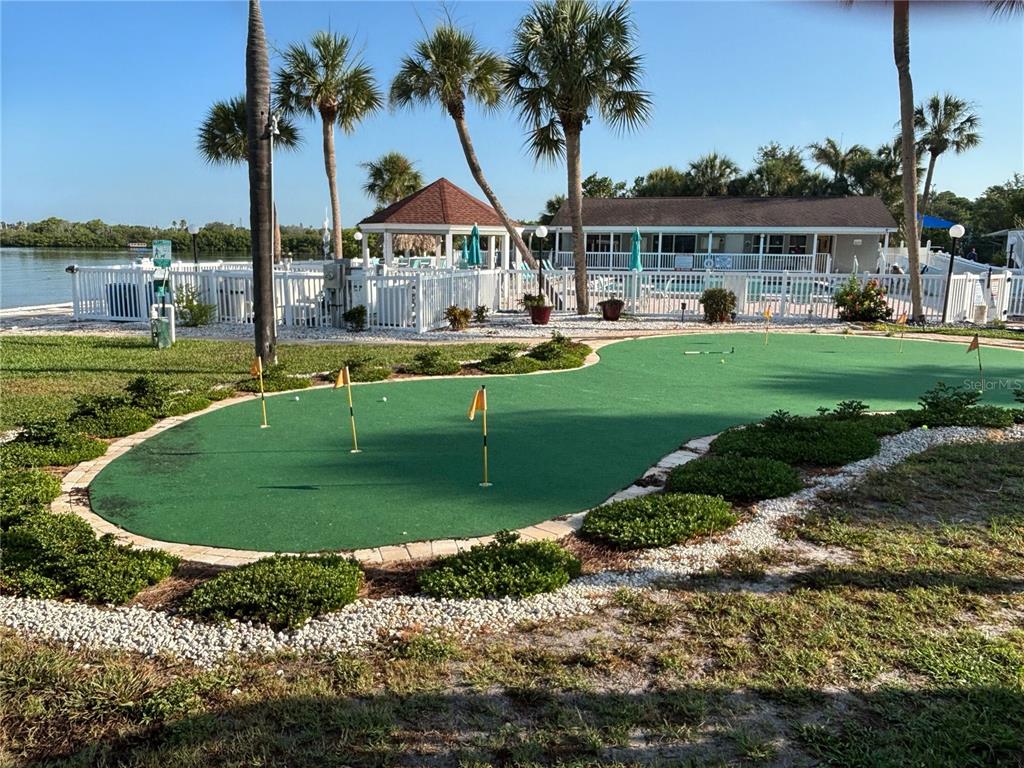 A putting green sits in the foreground of a waterfront community pool and gazebo area — 3640 41ST LANE S UNIT 72E, ST PETERSBURG, FL