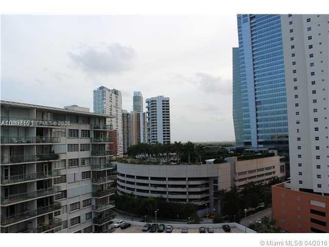 An exterior view shows a multi-story apartment building next to a parking garage and skyscrapers — 1402 Brickell Bay Dr # 1103, Miami FL 33131, MIAMI, FL