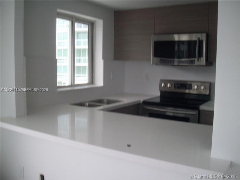 A modern kitchen features white countertops, stainless steel appliances, and wood-toned upper cabinets — 1402 Brickell Bay Dr # 1103, Miami FL 33131, MIAMI, FL