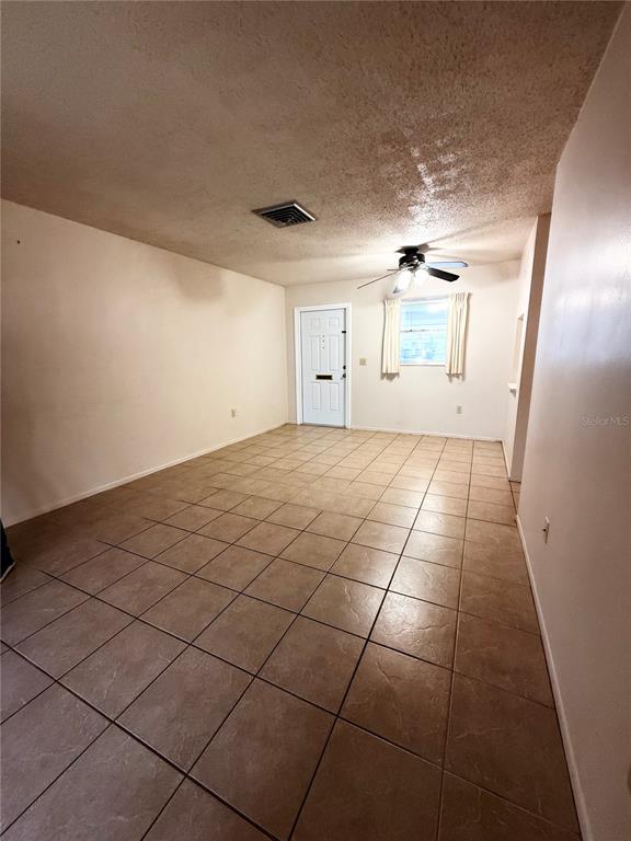 An empty living room features beige tile flooring, a ceiling fan, and a sliding glass door — 5994 HIBISCUS DRIVE, BRADENTON, FL