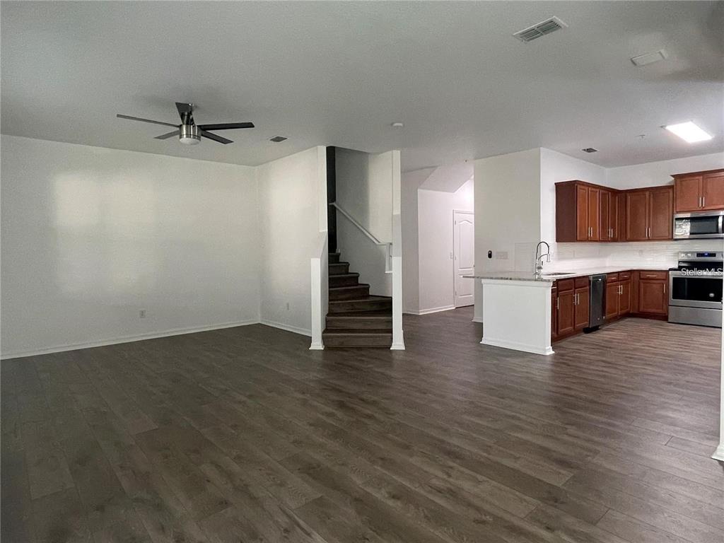 An open-concept living room features wood-look flooring, a staircase, and an adjacent kitchen with cabinets — 3723 SENECA CLUB LOOP UNIT 31-102, ORLANDO, FL