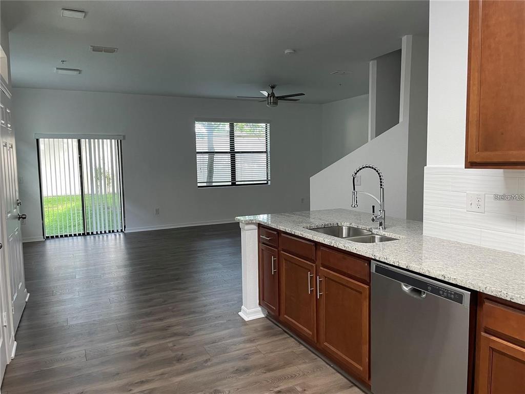 A kitchen with granite countertops and wood cabinets overlooks an open living area with flooring — 3723 SENECA CLUB LOOP UNIT 31-102, ORLANDO, FL