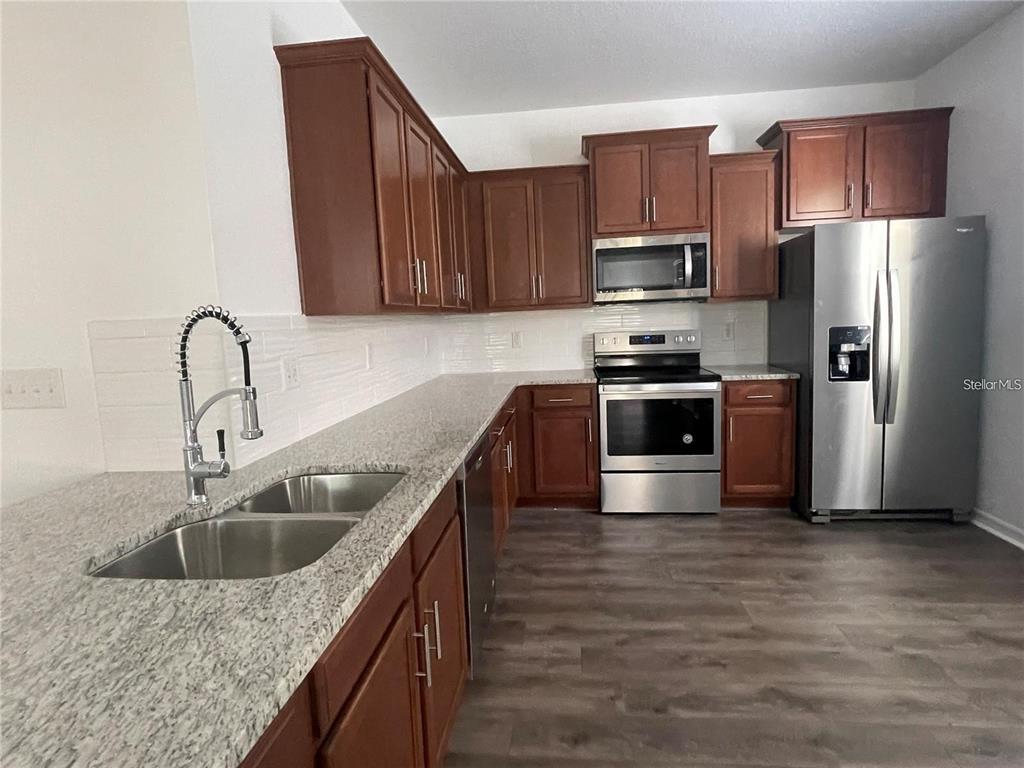 A kitchen featuring wood cabinets, granite countertops, stainless steel appliances, and wood-look flooring — 3723 SENECA CLUB LOOP UNIT 31-102, ORLANDO, FL