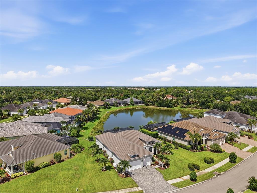An aerial view shows several suburban houses surrounding a central pond under a blue sky — 21253 CHATTAHOOCHEE AVENUE, VENICE, FL