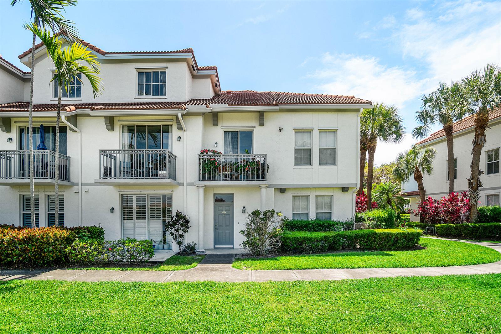A two-story townhouse with a gray front door, balconies, and surrounding landscaping — 2052 Alta Meadows Lane Apt 2212, Delray Beach FL 33444, DELRAY BEACH, FL