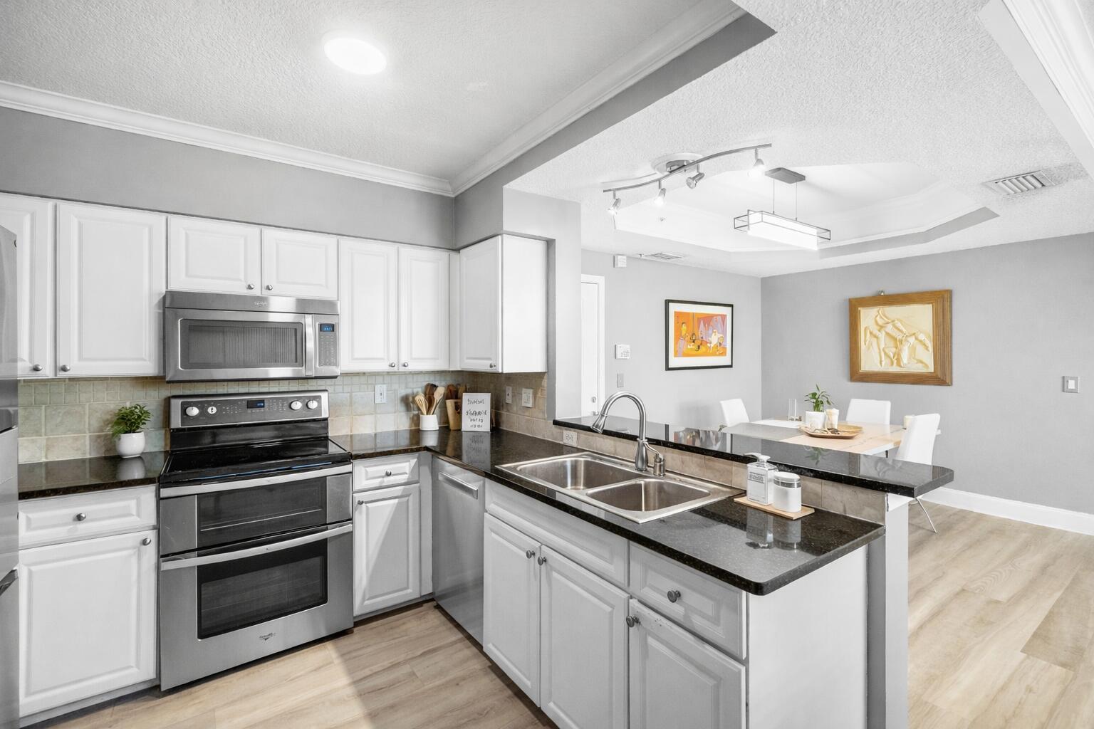A kitchen with white cabinets, stainless steel appliances, and dark countertops opens to a dining area — 2052 Alta Meadows Lane Apt 2212, Delray Beach FL 33444, DELRAY BEACH, FL