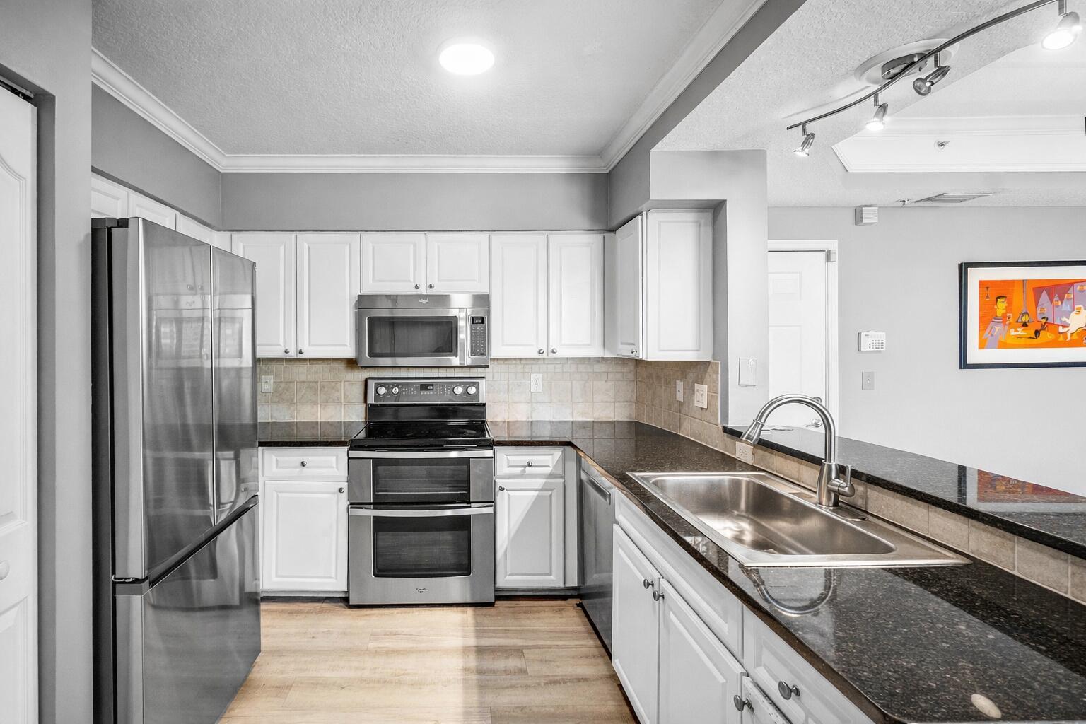 A kitchen features white cabinets, stainless steel appliances, dark granite countertops, and light wood flooring — 2052 Alta Meadows Lane Apt 2212, Delray Beach FL 33444, DELRAY BEACH, FL