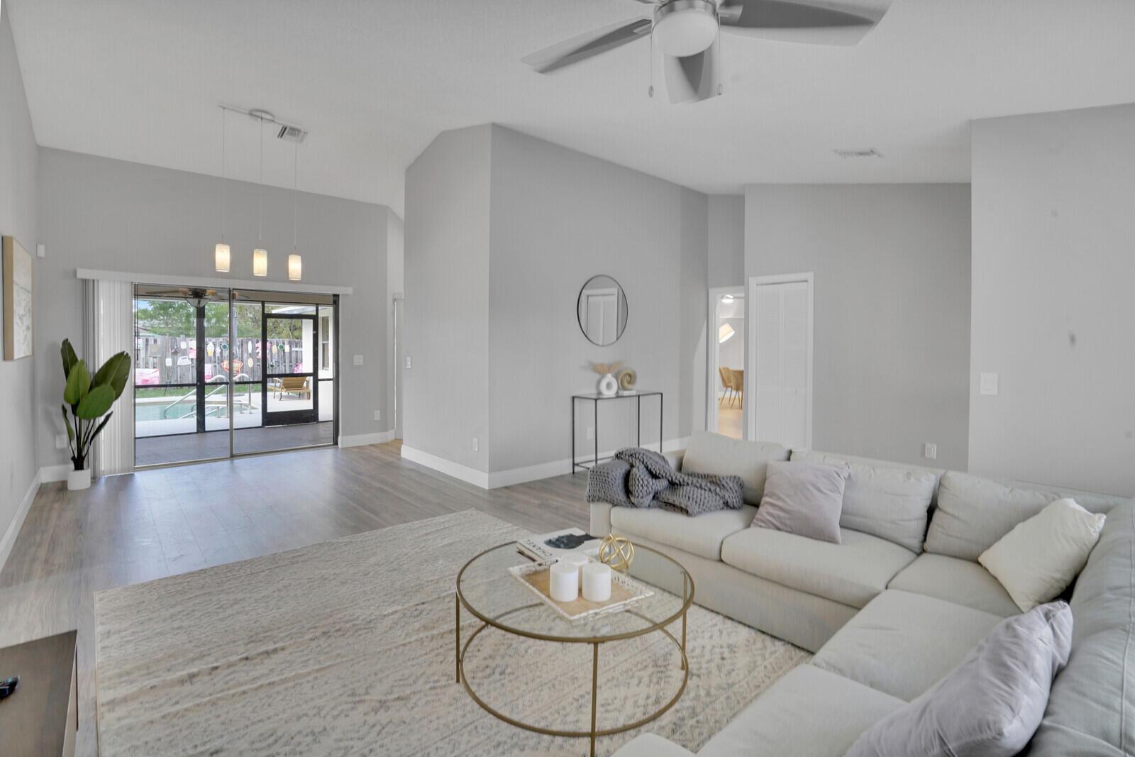 A living room with a sectional sofa, glass coffee table, and sliding doors to a pool — 13834 Geranium Place, Wellington FL 33414, WELLINGTON, FL