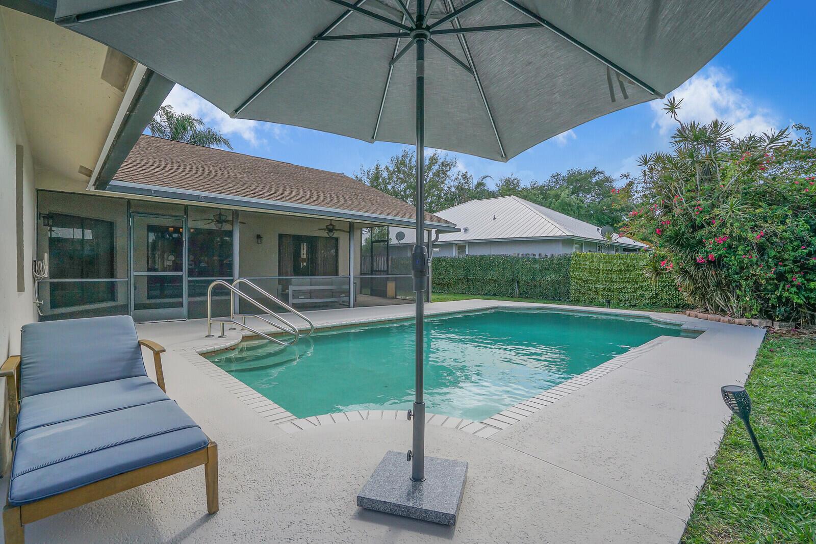 A backyard swimming pool with a patio, lounge chair, and umbrella next to a house — 13834 Geranium Place, Wellington FL 33414, WELLINGTON, FL