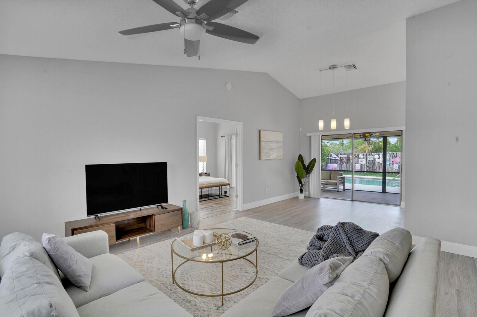 A living room with a vaulted ceiling, light wood floors, and a sliding glass door — 13834 Geranium Place, Wellington FL 33414, WELLINGTON, FL