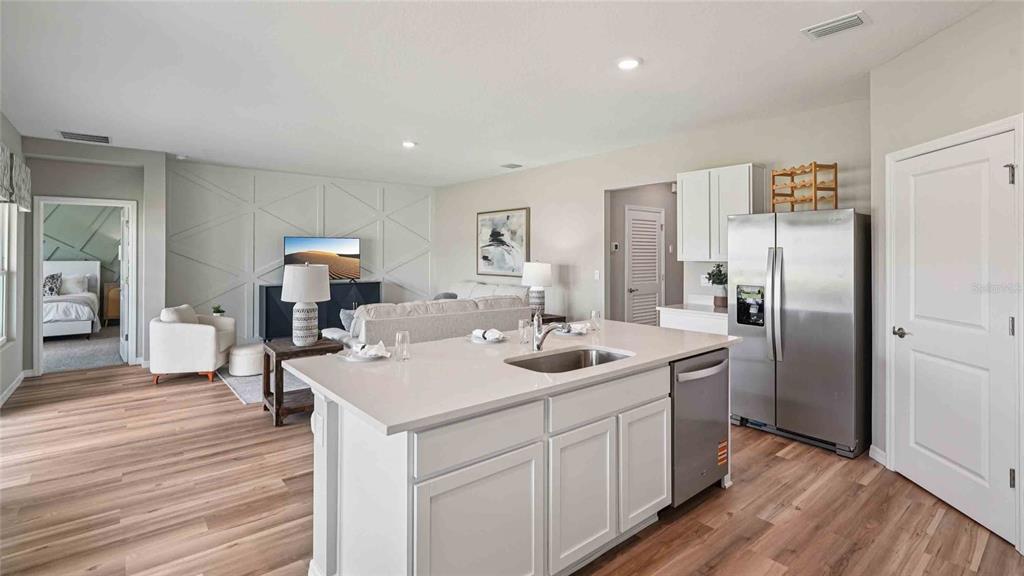 A kitchen island with a sink overlooks a living room featuring a geometric accent wall — 4623 KONA CIRCLE, SPRING HILL, FL