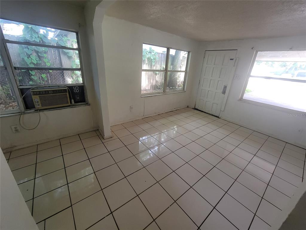 An empty room with white tile flooring, multiple windows, and a white exterior door — 731 23RD STREET UNIT 3, ORLANDO, FL