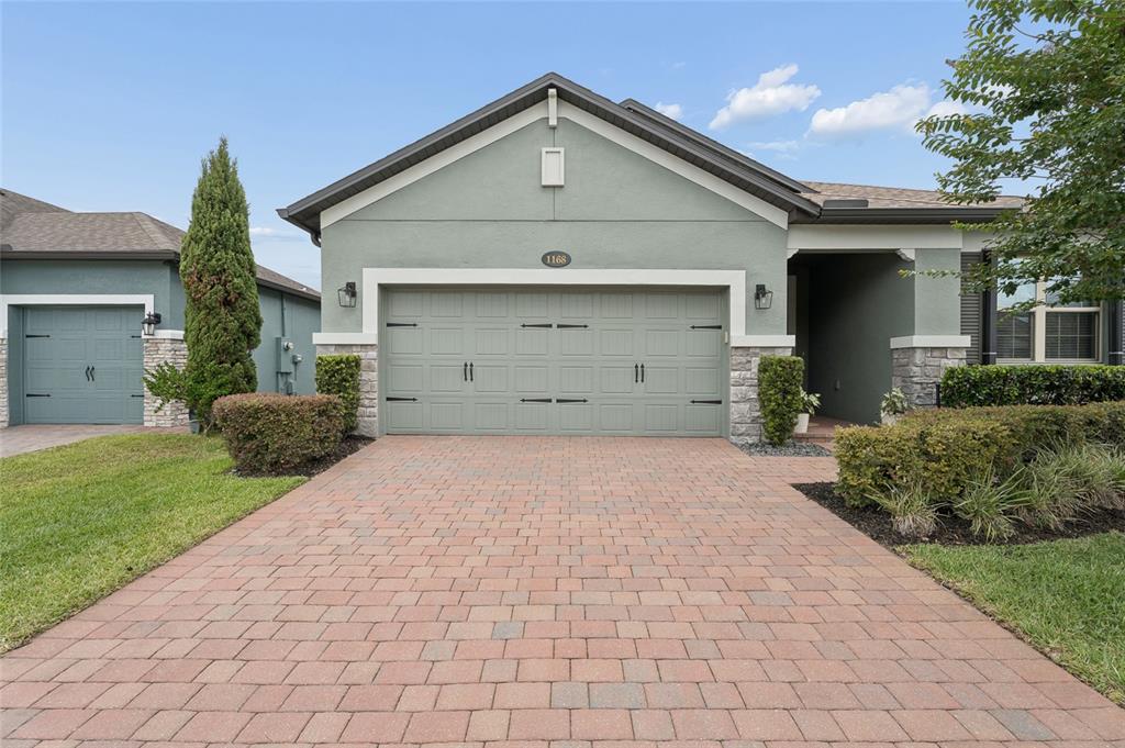 A single-story house with a sage green exterior, stone accents, and a brick paver driveway — 1168 NARCOOSSEE DEL SOL, ST CLOUD, FL