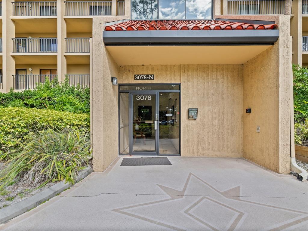 The exterior entrance of a multi-story building features a glass door and a tiled roof — 3078 EASTLAND BOULEVARD UNIT 309, CLEARWATER, FL