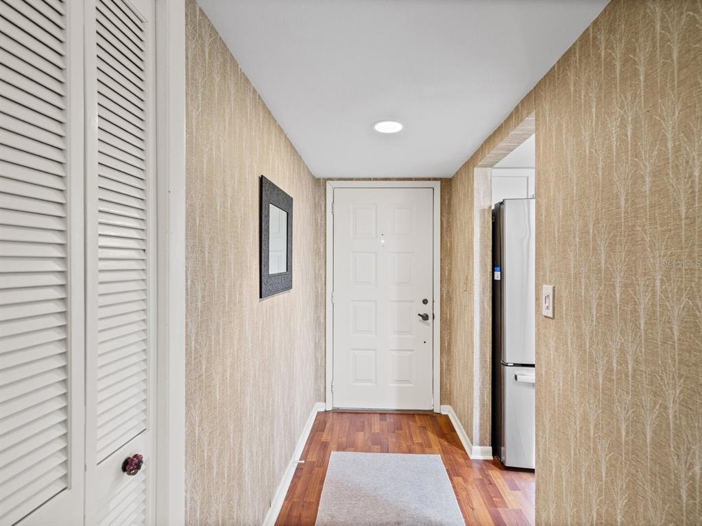 A hallway with wood-look flooring, textured wallpaper, a white door, and a closet door — 3078 EASTLAND BOULEVARD UNIT 309, CLEARWATER, FL