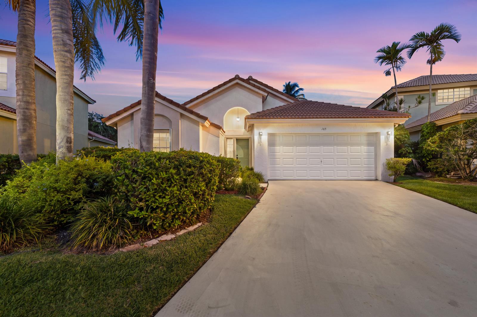A single-story house with a white garage, tiled roof, and palm trees at sunset — 165 St Michaels Court, Jupiter FL 33458, JUPITER, FL