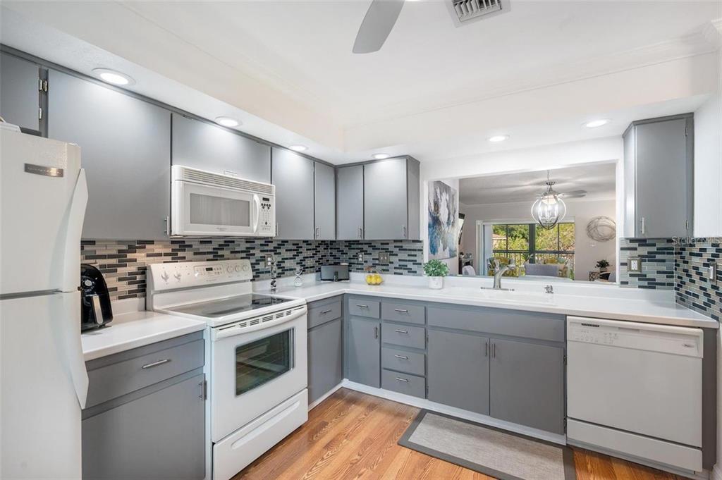 A kitchen with gray cabinets, white appliances, a tiled backsplash, and wood flooring — 2700 NEBRASKA AVENUE UNIT 5-203, PALM HARBOR, FL