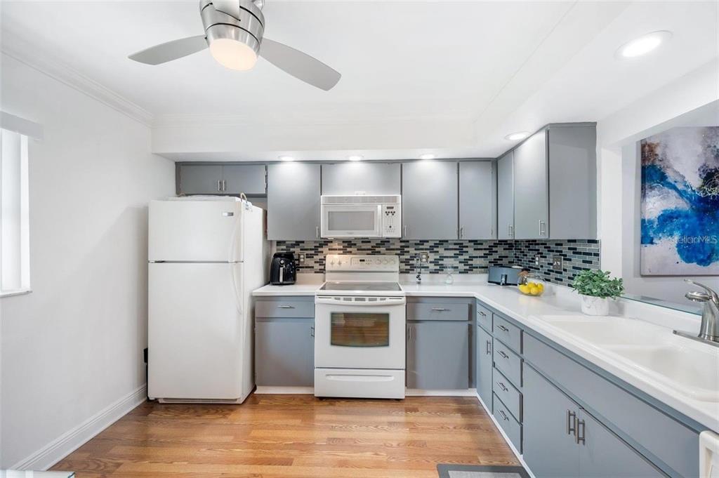 A kitchen features gray cabinets, white appliances, a mosaic tile backsplash, and hardwood flooring — 2700 NEBRASKA AVENUE UNIT 5-203, PALM HARBOR, FL