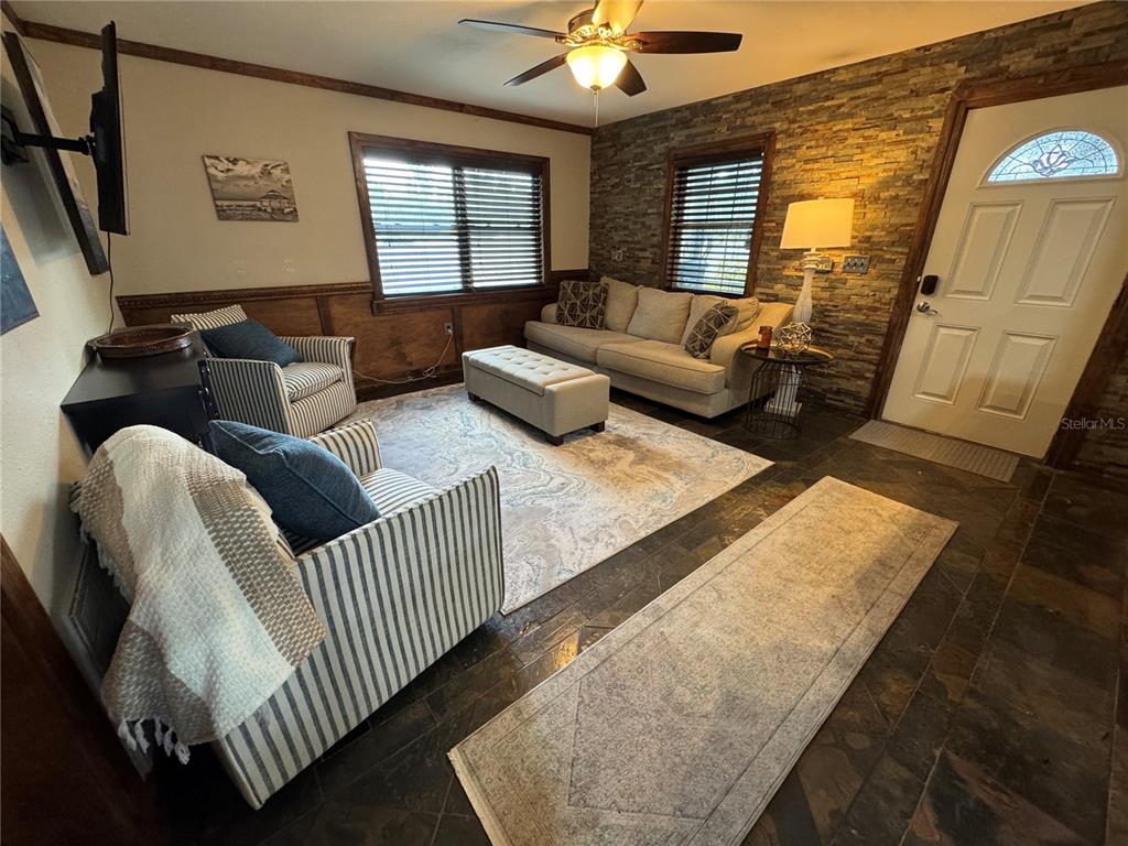 A living room features a stone accent wall, wood wainscoting, tile flooring, and striped furniture — 2751 72ND AVENUE DRIVE E, SARASOTA, FL