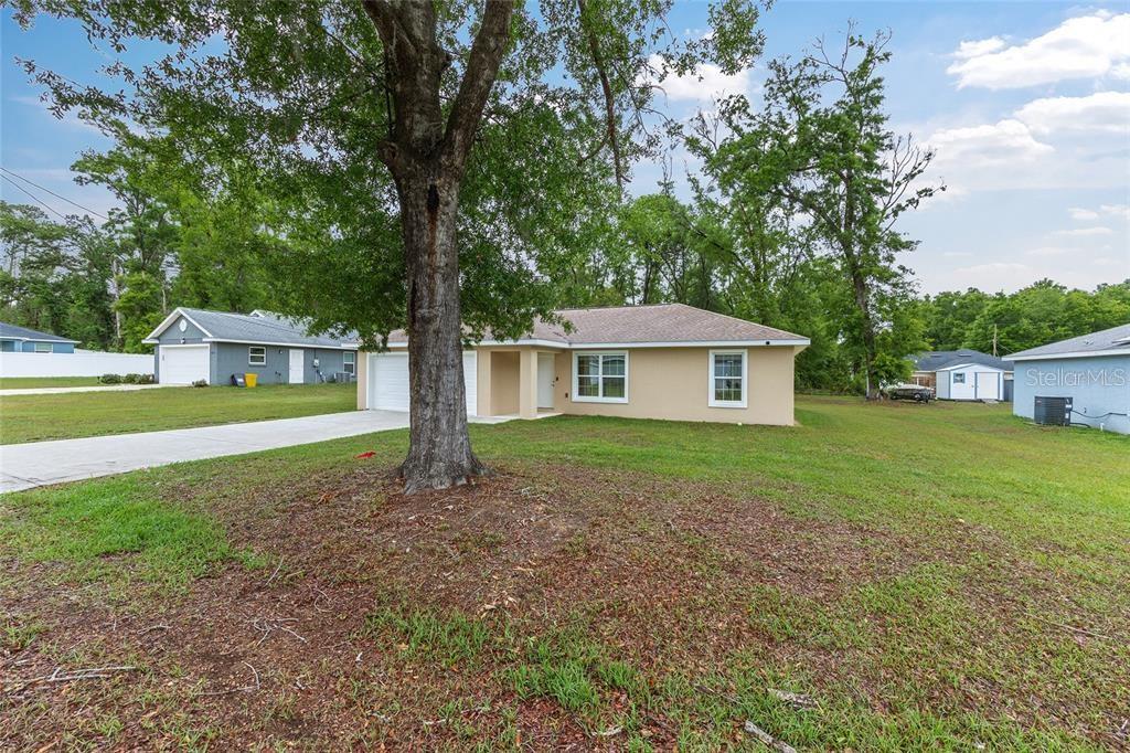 A single-story house with a tan exterior, white trim, and a two-car garage — 6975 SE 124TH LANE, BELLEVIEW, FL