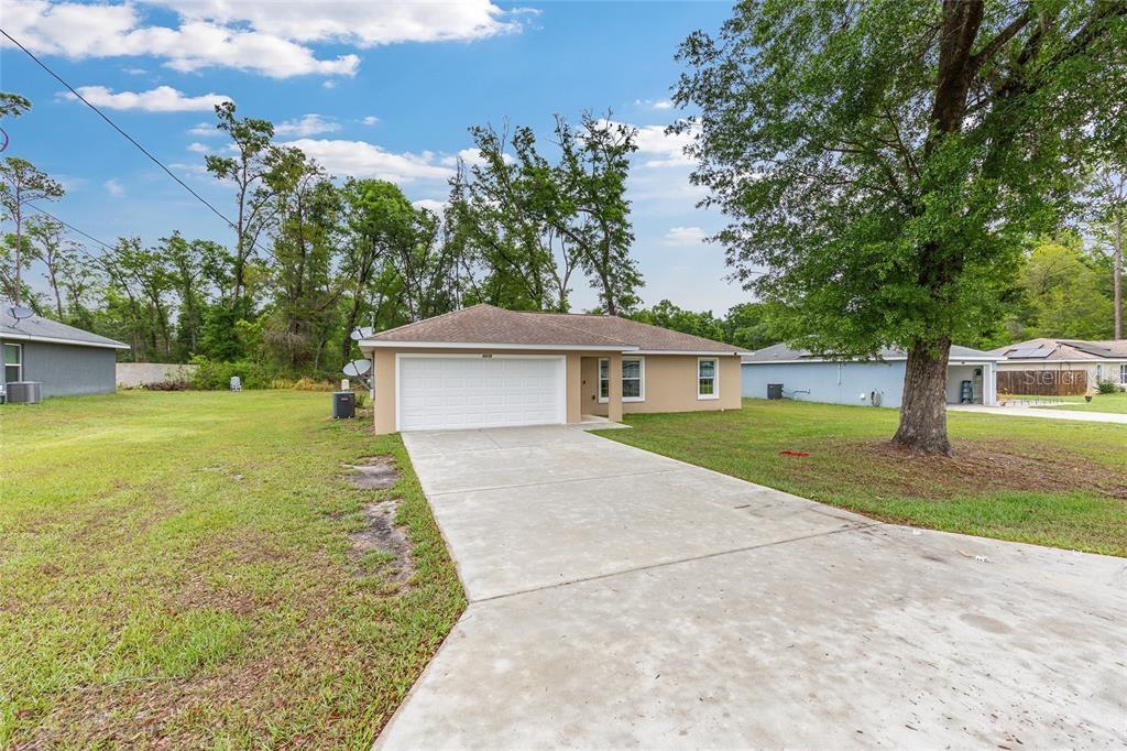 A tan single-story house with a white garage door and a concrete driveway — 6975 SE 124TH LANE, BELLEVIEW, FL