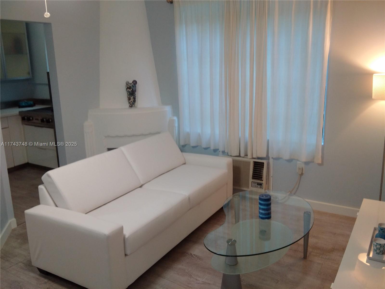 A living room features a white sofa, a glass coffee table, and an adjacent kitchen — 1525 Meridian Ave # 104, Miami Beach FL 33139, MIAMI BEACH, FL
