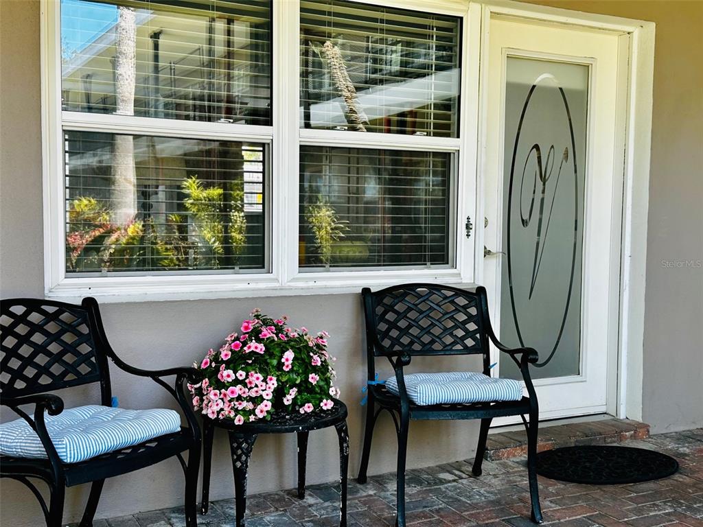 A patio features two black metal chairs with striped cushions and a potted flower arrangement — 1101 VICTORIA DRIVE UNIT 7, DUNEDIN, FL