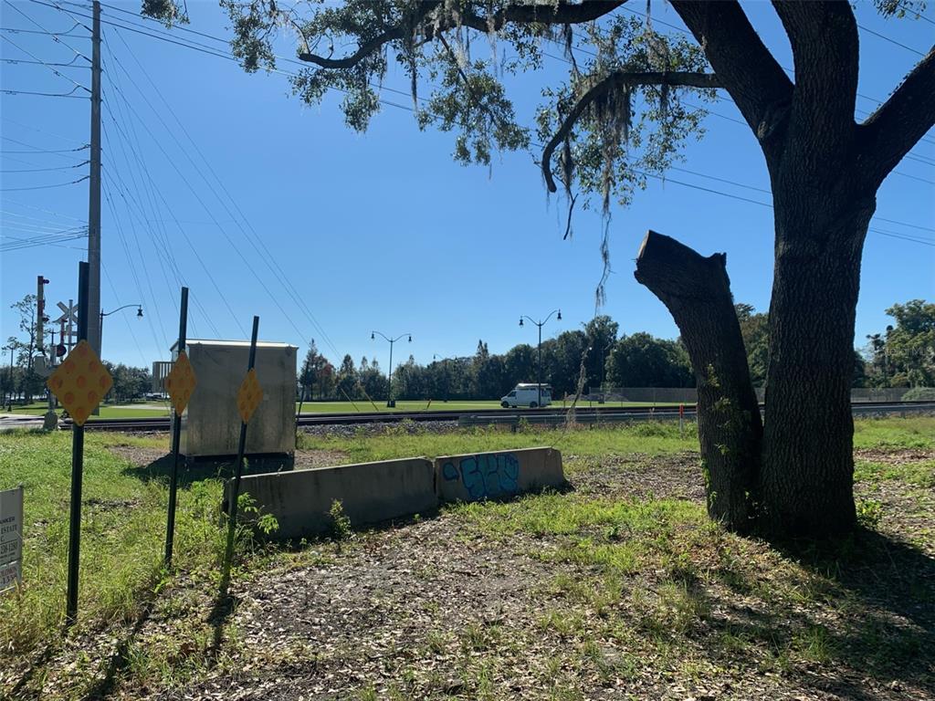 A view of a grassy lot with a large tree, railroad tracks, and utility equipment — S VERNON AVENUE, KISSIMMEE, FL