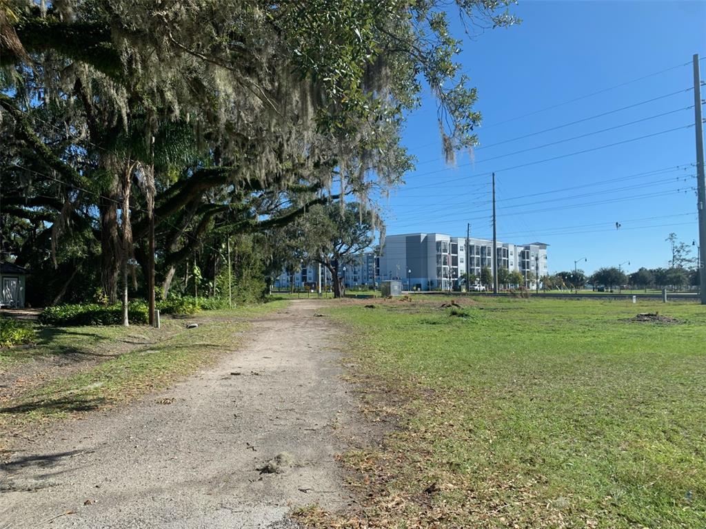A dirt path leads through a grassy field toward a large apartment building under trees — S VERNON AVENUE, KISSIMMEE, FL