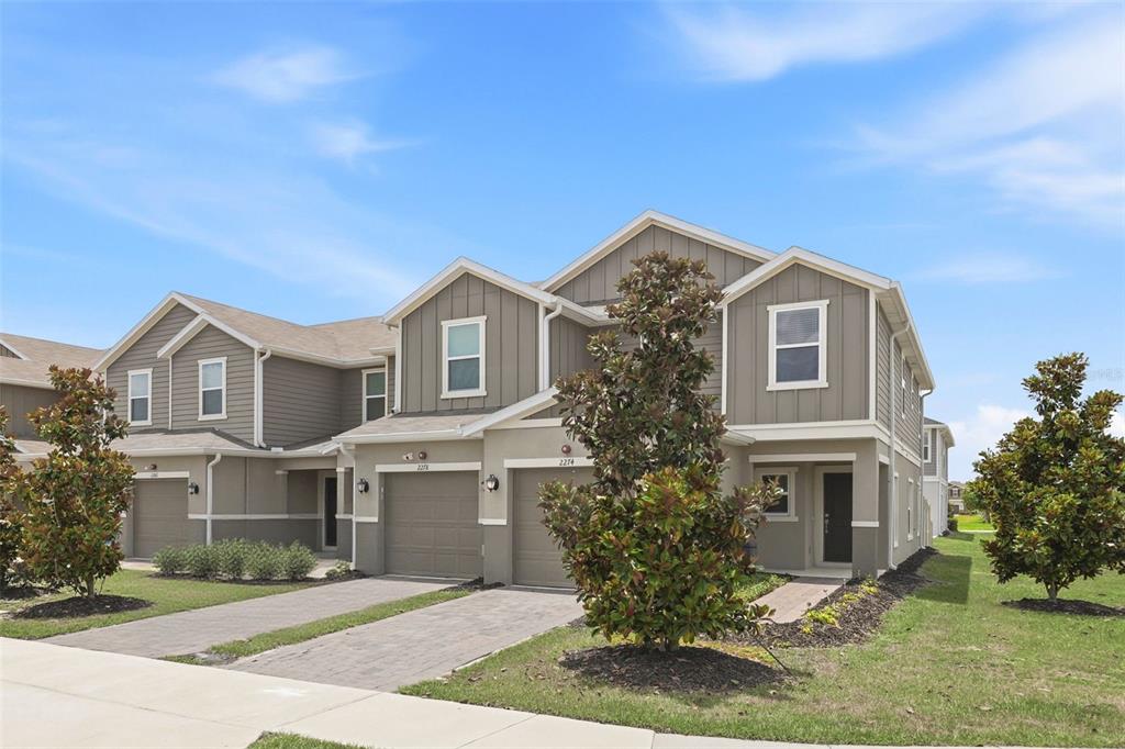 A two-story townhouse exterior with a paved driveway, two garage doors, and a small lawn — 2274 CARRABELLE WAY, SANFORD, FL