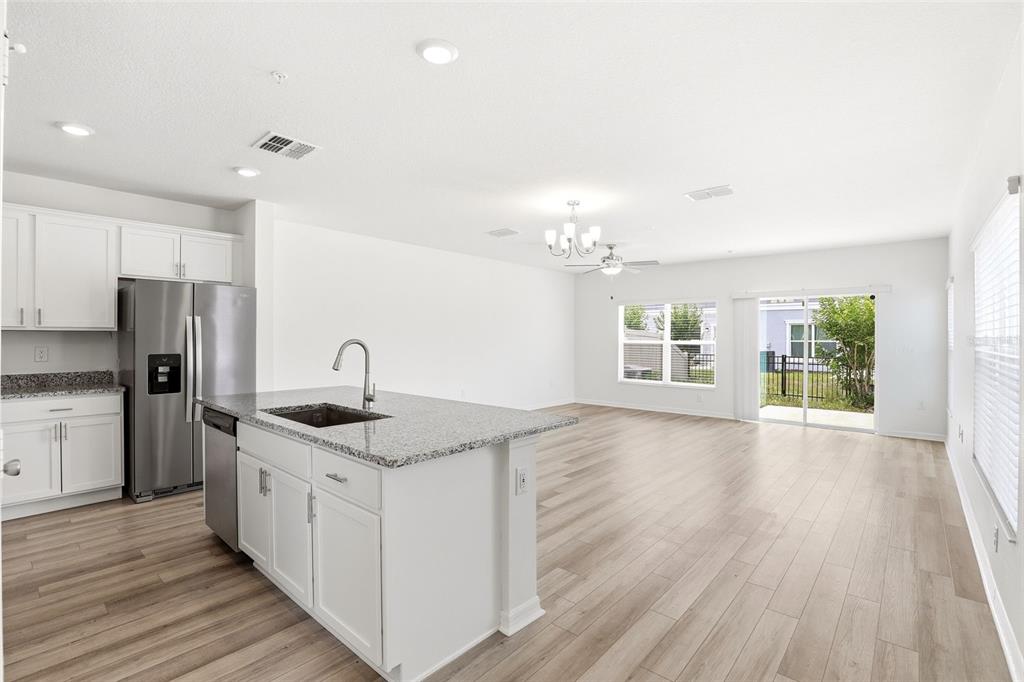 A kitchen with a granite island and stainless steel appliances opens to a living area — 2274 CARRABELLE WAY, SANFORD, FL