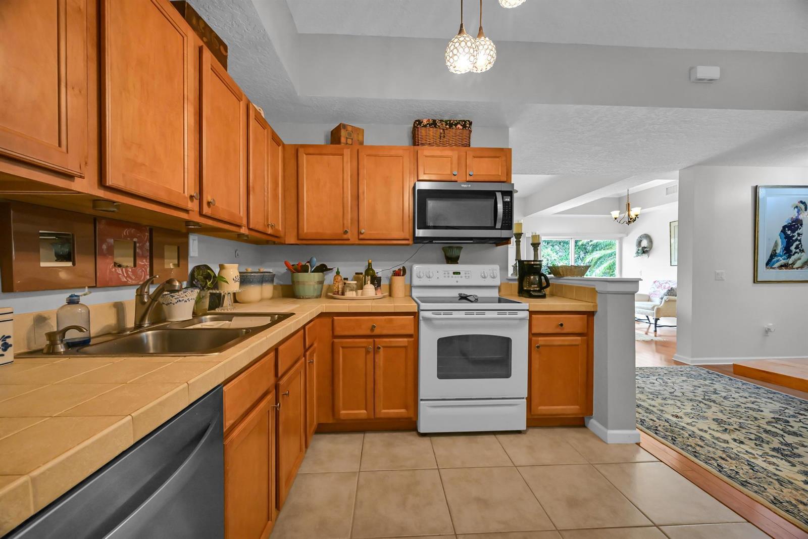 A kitchen features wood cabinets, tile countertops, a white stove, and a stainless steel dishwasher — 568 7th Square, Vero Beach FL 32962, VERO BEACH, FL