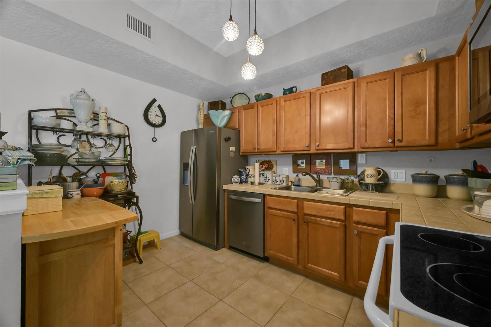 A kitchen features wood cabinets, stainless steel appliances, tile countertops, and a metal baker's rack — 568 7th Square, Vero Beach FL 32962, VERO BEACH, FL